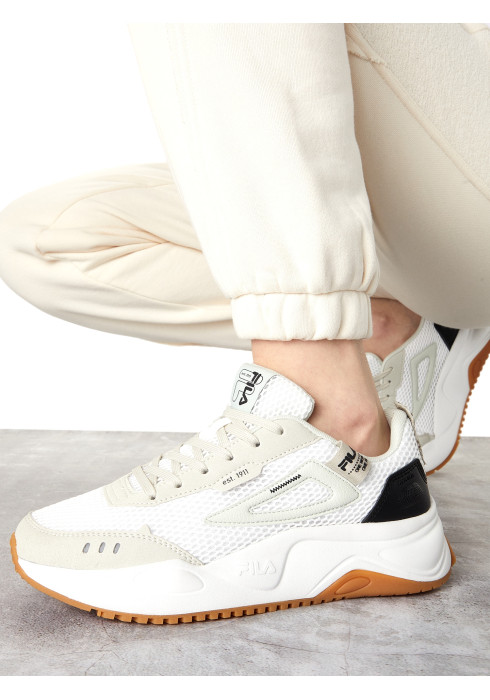 Жіночі білі кросівки FILA в стилі dad shoe на нозі у світлому спортивному костюмі