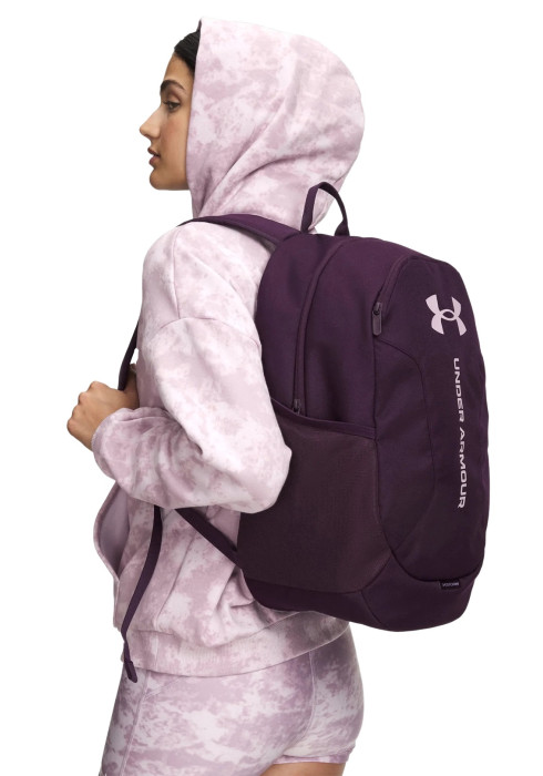 Жінка у світлому худі з фіолетовим рюкзаком Under Armour Hustle Lite Backpack збоку на білому тлі