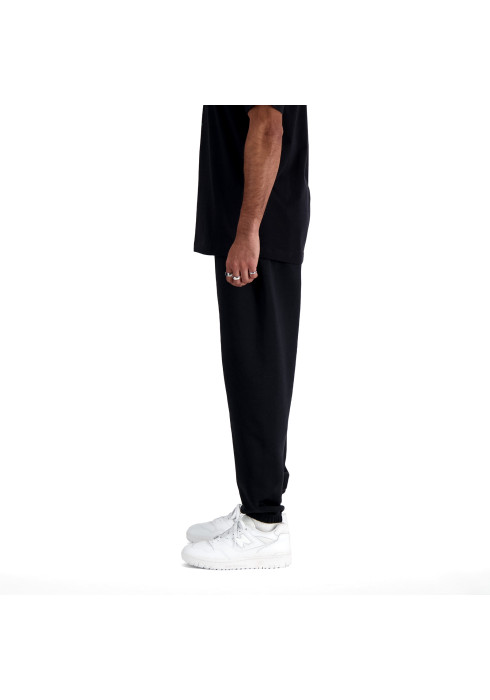 Чоловік у чорних спортивних штанях New Balance Sport Essentials та білих кросівках студійний вигляд збоку на білому тлі